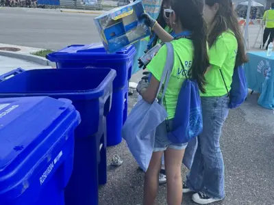 Two volunteers place cardboard in a recycling bin